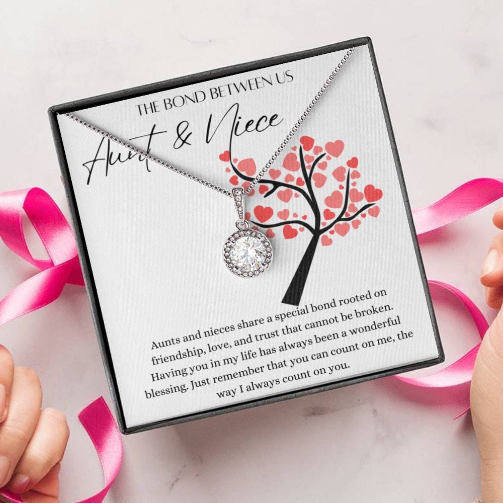 A person unwrapping necklace gift, with a big cubic zirconia crystal pendant and a white gold finish, with a message card for aunts and nieces.