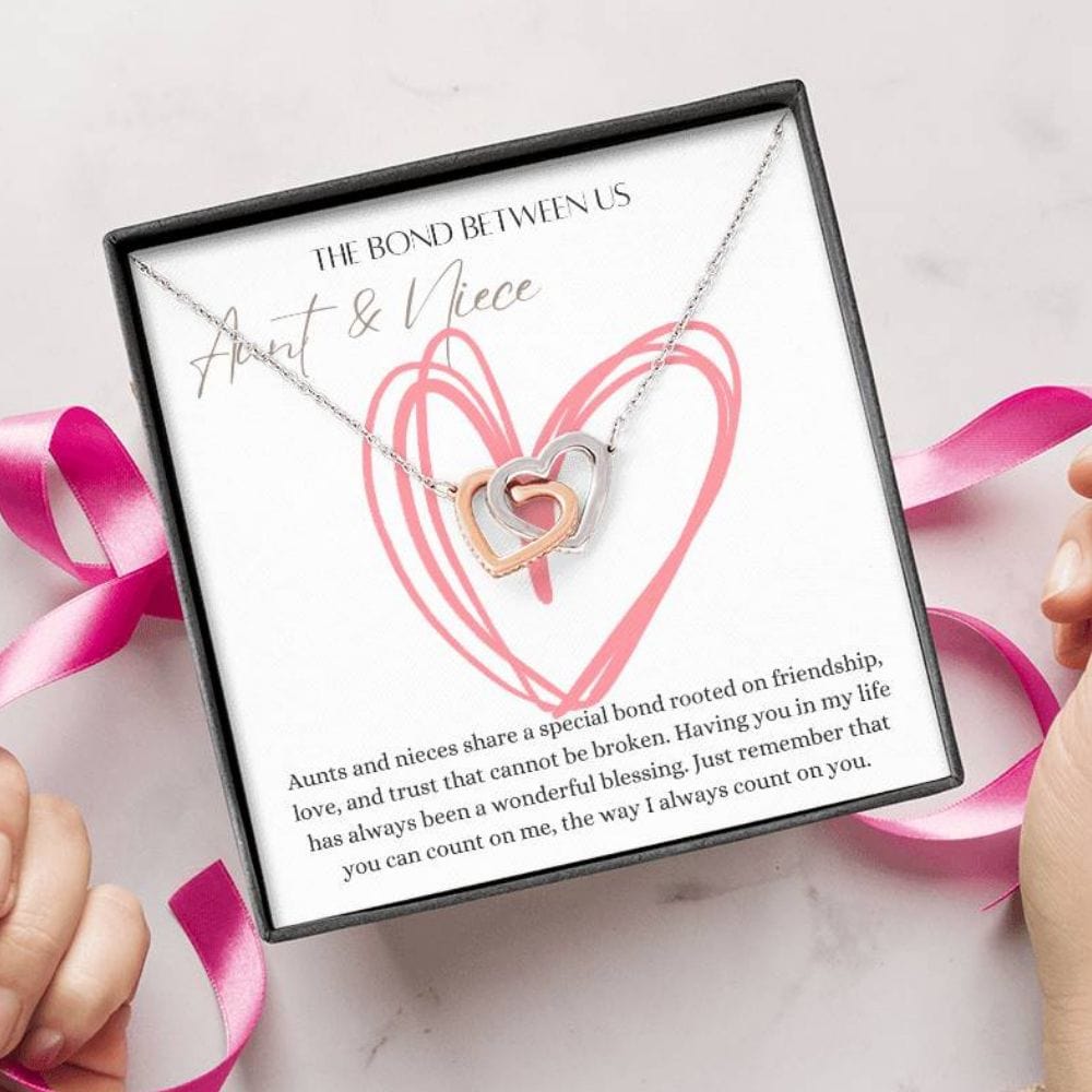 A person unwrapping a necklace with two connected hearts embellished with with cubic zirconia crystals with a message card for aunts and nieces.