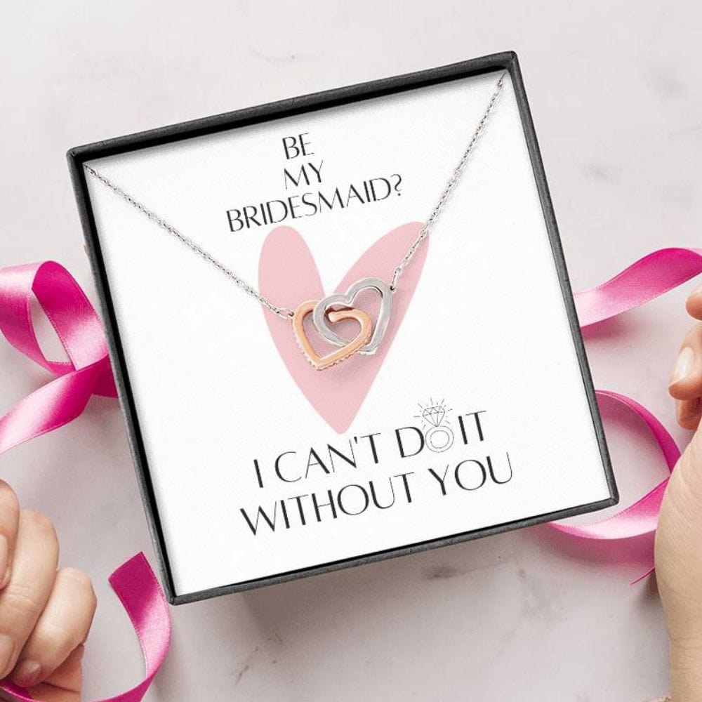 A person unwrapping a necklace with two connected hearts embellished with cubic zirconia crystals with a message card for bridesmaids.
