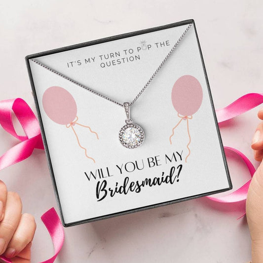 A person unwrapping a necklace gift, with a big cubic zirconia crystal pendant and a white gold finish, with a message card to bridesmaids.