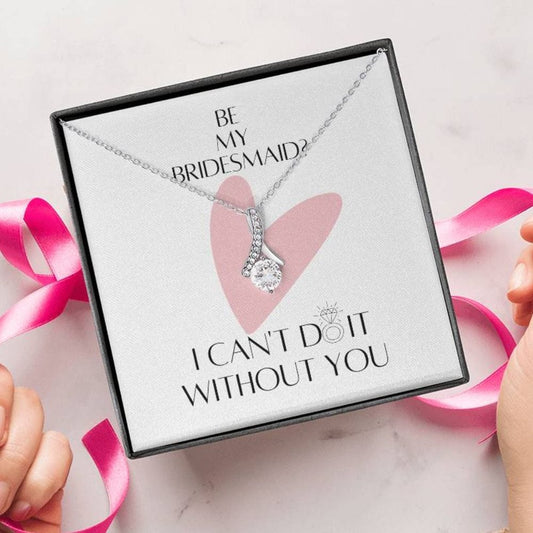 A person unwrapping a necklace gift with ribbon shaped pendant with cubic zirconia crystals and white gold finish with a message card for bridesmaids.