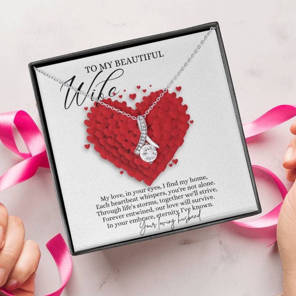 A person unwrapping a necklace gift with ribbon shaped pendant with cubic zirconia crystals and white gold finish, with a message card to my beautiful wife.