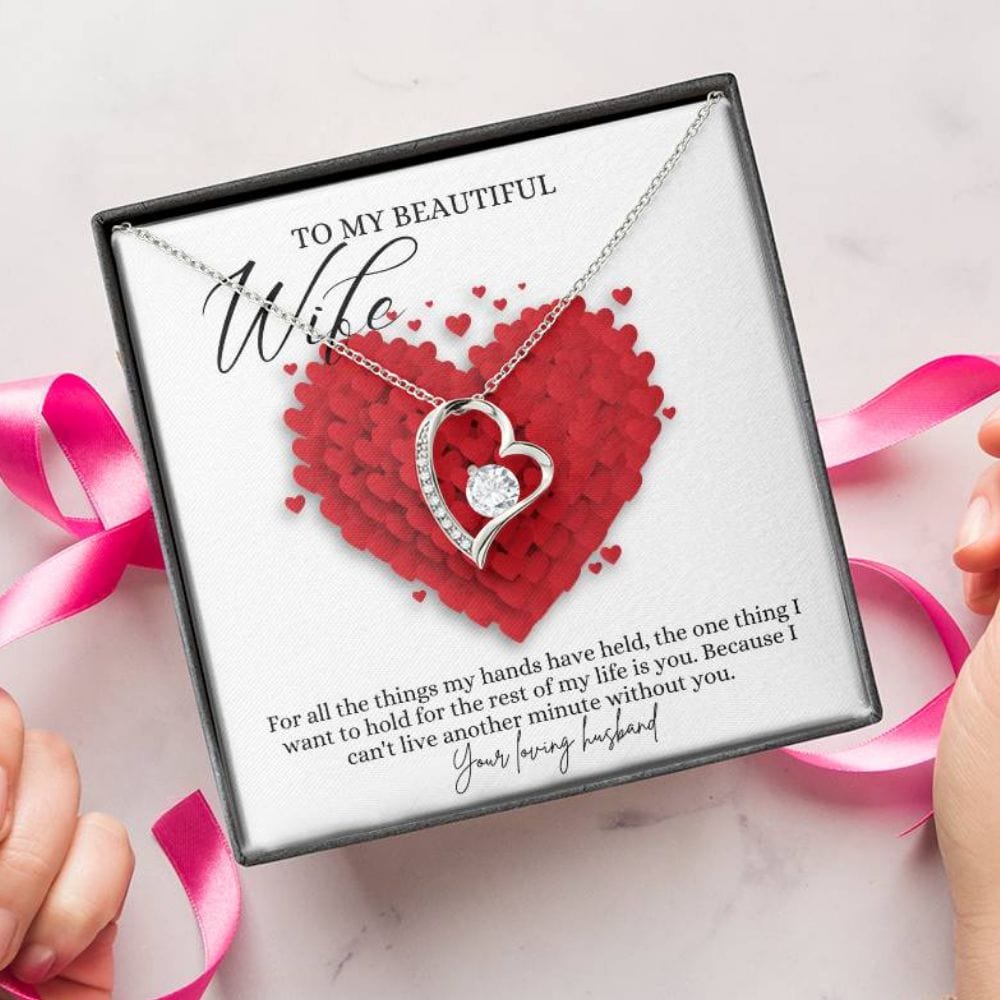 A person unwrapping a jewelry box with a white gold finish necklace gift, featuring a stunning 6.5mm CZ crystal surrounded by a polished heart pendant embellished with smaller crystals, with a message card to my beautiful wife.