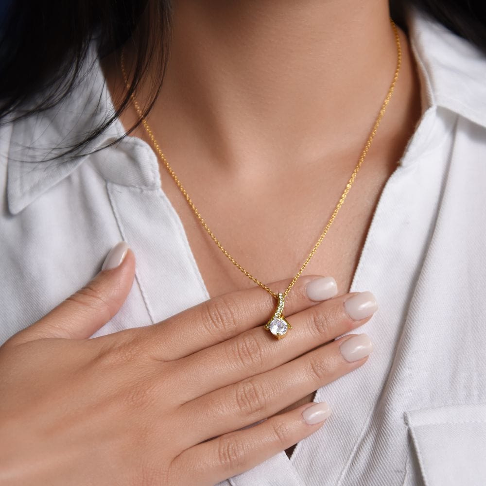 A woman touching a necklace on her neck with ribbon shaped pendant with cubic zirconia crystals and a gold finish.