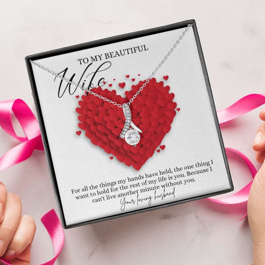 A person unwrapping a necklace gift with ribbon shaped pendant with cubic zirconia crystals and white gold finish, with a message card to my beautiful wife.