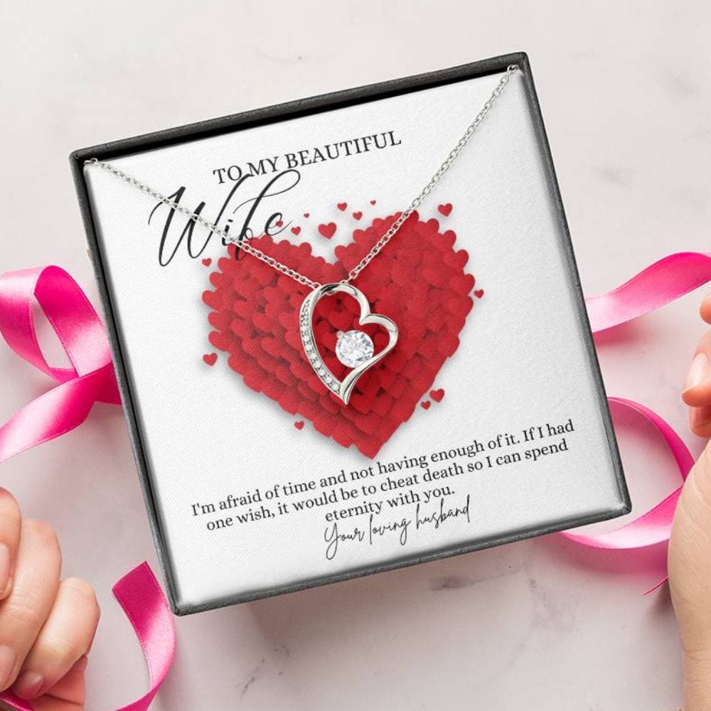 A person unwrapping a jewelry box with a white gold finish necklace gift, featuring a stunning 6.5mm CZ crystal surrounded by a polished heart pendant embellished with smaller crystals, with a message card to my beautiful wife.