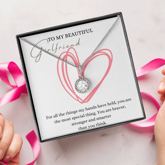 A person unwrapping a necklace gift, with a big cubic zirconia crystal pendant and a white gold finish, with a message card to my beautiful girlfriend.