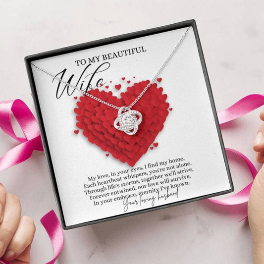 A person unwrapping a jewelry box with a white gold finish necklace gift, with a knot pendant embellished with premium cubic zirconia crystals, and a message card to my beautiful wife.
