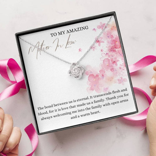 A person unwrapping a jewelry box with a white gold finish necklace gift, with a knot pendant embellished with premium cubic zirconia crystals, and a message card to my amazing mother-in-law.