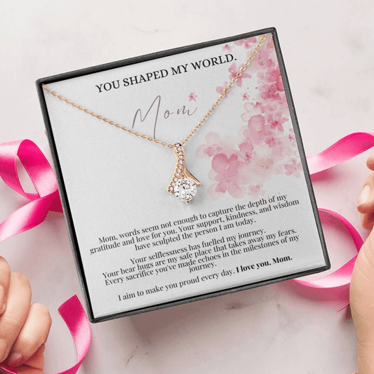 A person unwrapping a necklace gift with ribbon shaped pendant with cubic zirconia crystals and white gold finish, with a mother's day message card.