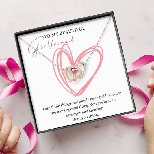 A person unwrapping a necklace gift, with two connected hearts embellished with cubic zirconia crystals and white gold finish, with a message card, to my beautiful girlfriend