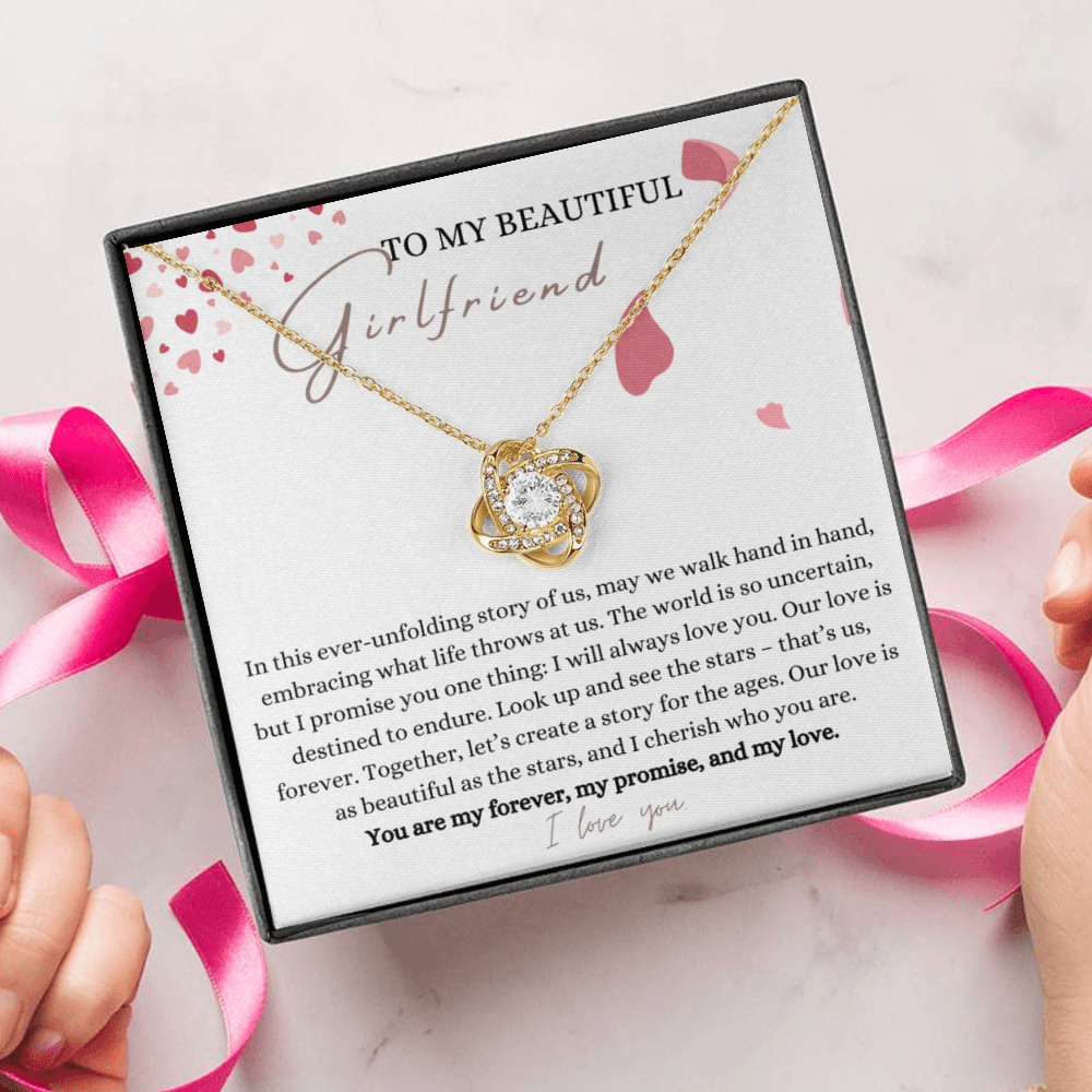 A person unwrapping a jewelry box with a white gold finish necklace gift, with a knot pendant embellished with premium cubic zirconia crystals, and a message card to my beautiful girlfriend.
