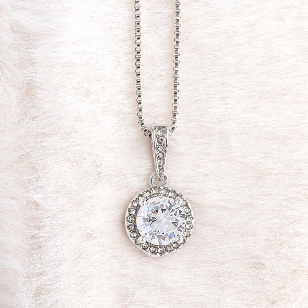 A necklace with a gold finish and a big cubic zirconia crystal pendant laying on a white furry carpet.