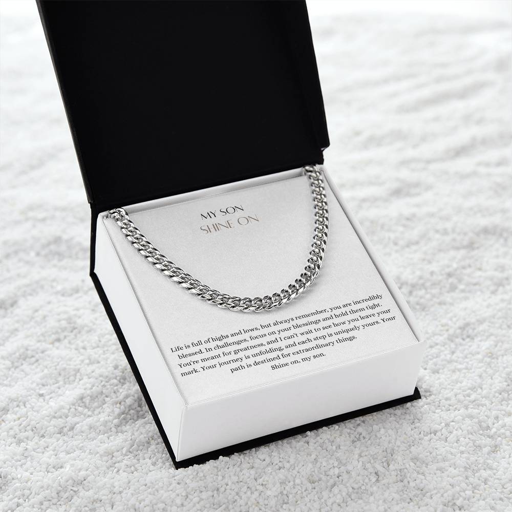 A Cuban chain necklace gift and a white gold finish, with a message card that says to my son, in a Jewelry box on a white carpet.