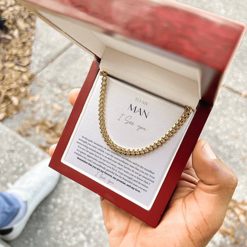 A man holding a mahogany Jewelry box. with a Cuban chain necklace gift with a yellow gold finish and a message card that says to my man.