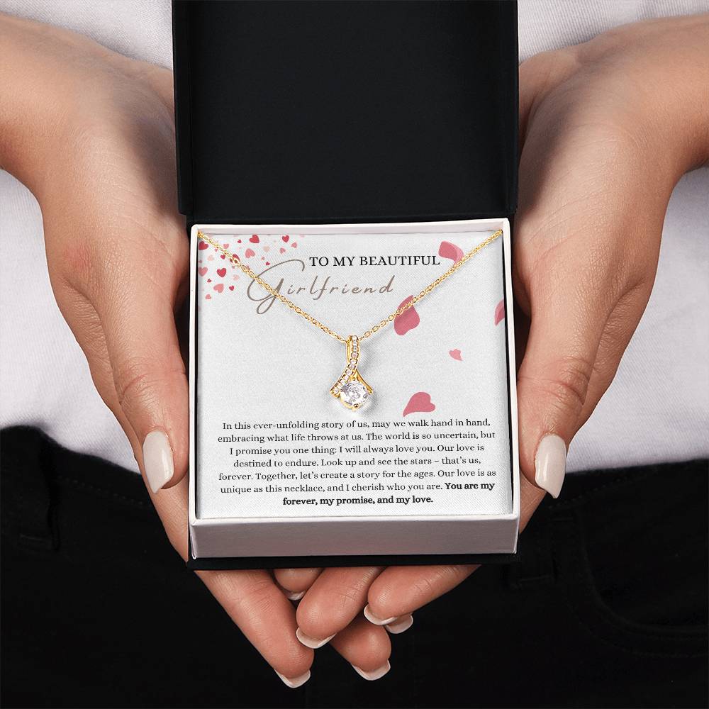 A woman presenting a Jewelry gift box with a necklace with ribbon shaped pendant made from cubic zirconia crystals and a gold finish, with a message card to my beautiful girlfriend.