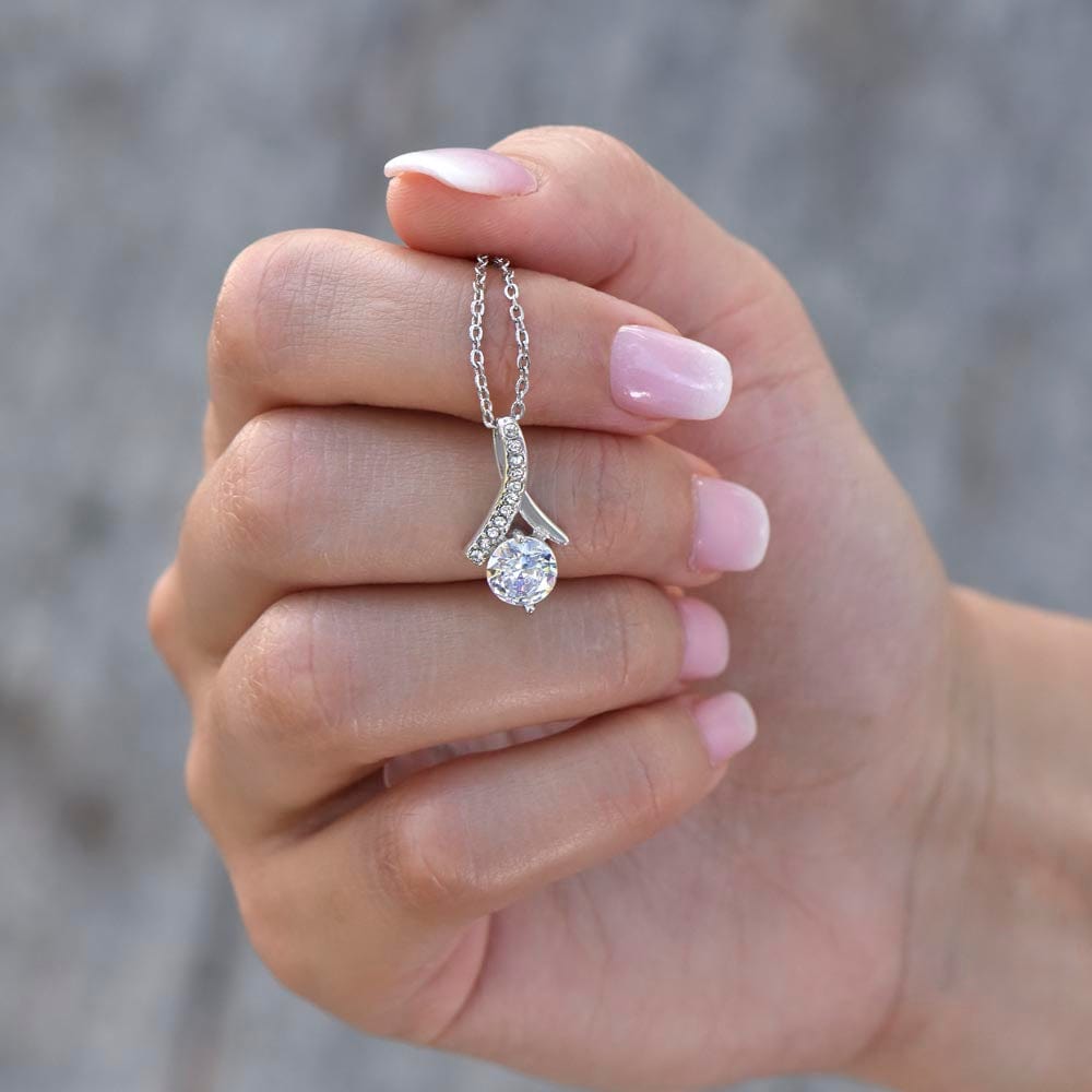 A woman holding a necklace with ribbon shaped pendant with cubic zirconia crystals and a white gold finish.