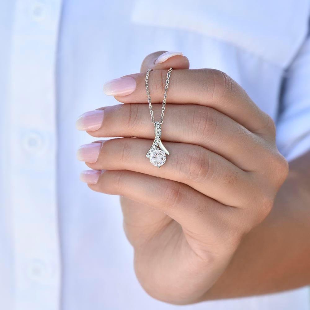 A woman holding a necklace with ribbon shaped pendant with cubic zirconia crystals and a white gold finish.
