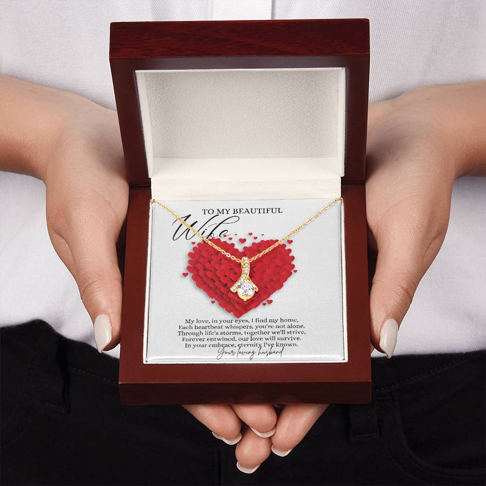 A woman presenting a mahogany Jewelry gift box with a necklace with ribbon shaped pendant made from cubic zirconia crystals and a gold finish, with a message card to my beautiful wife.