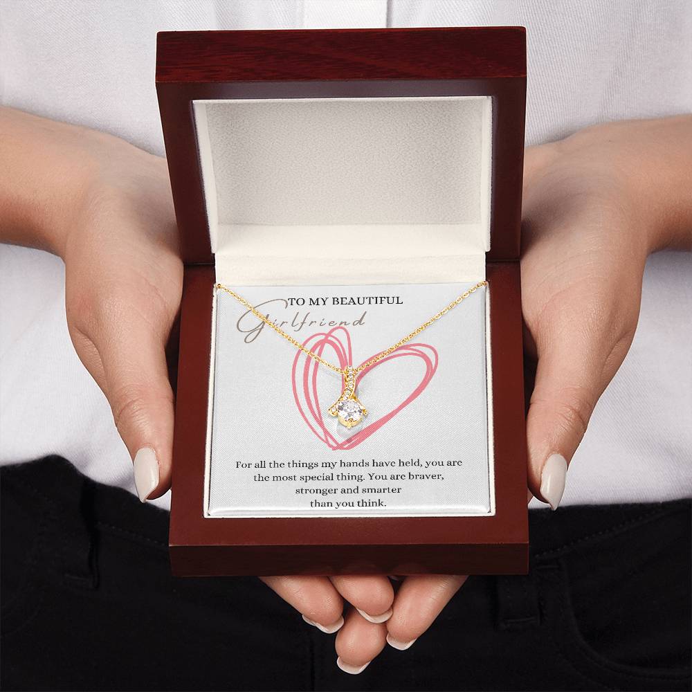 A woman presenting a mahogany Jewelry gift box with a necklace with ribbon shaped pendant made from cubic zirconia crystals and a gold finish, with a message card to my beautiful girlfriend.