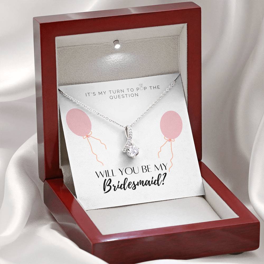 A necklace gift with ribbon shaped pendant with cubic zirconia crystals and white gold finish, with a message card to bridesmaids in a mahogany Jewelry box.