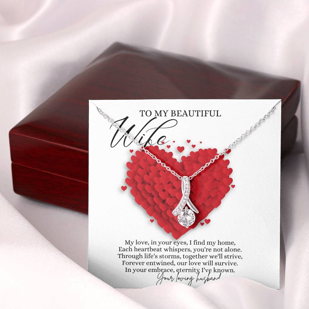 A necklace gift with ribbon shaped pendant with cubic zirconia crystals and white gold finish, with a message card to my beautiful wife next to a mahogany Jewelry box.