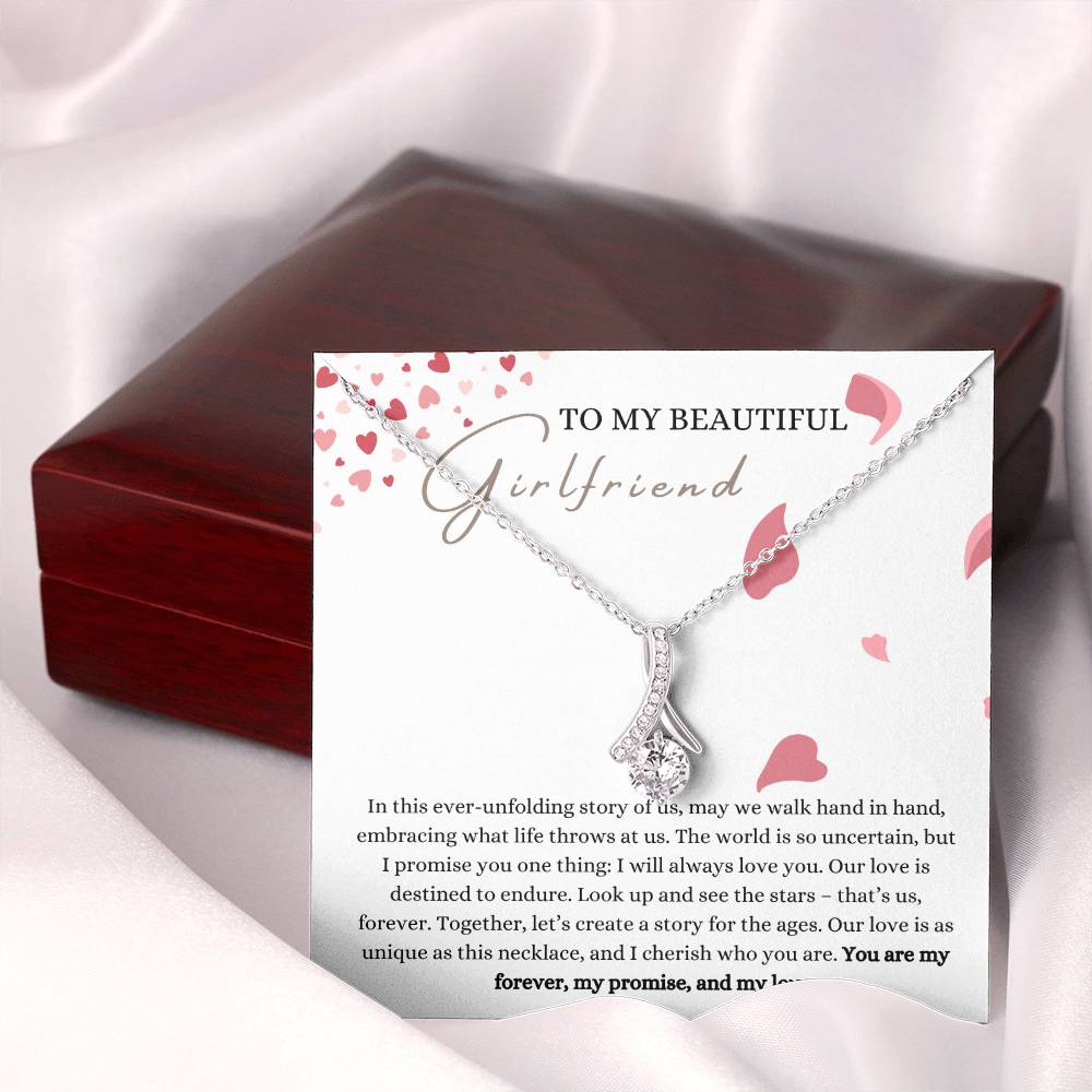 A necklace gift with ribbon shaped pendant with cubic zirconia crystals and white gold finish, with a message card to my beautiful girlfriend next to a mahogany Jewelry box.