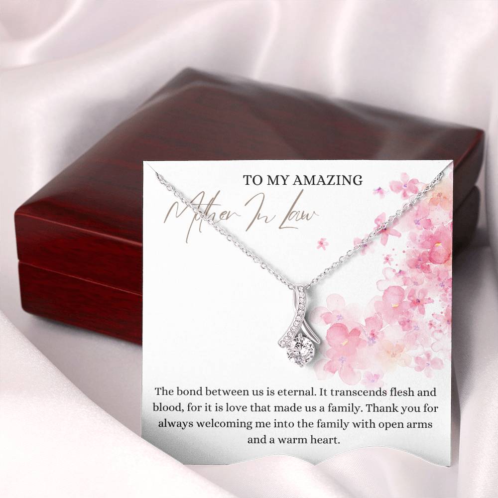 A necklace gift with ribbon shaped pendant with cubic zirconia crystals and white gold finish, with a message card to my mother in law next to a mahogany Jewelry box.