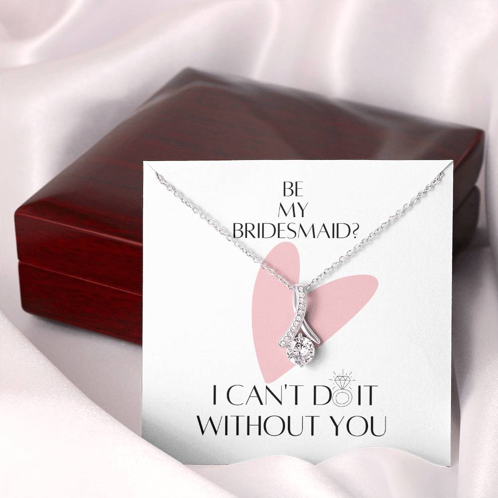 A necklace gift with ribbon shaped pendant with cubic zirconia crystals and white gold finish with a message card next to a mahogany gift box.
