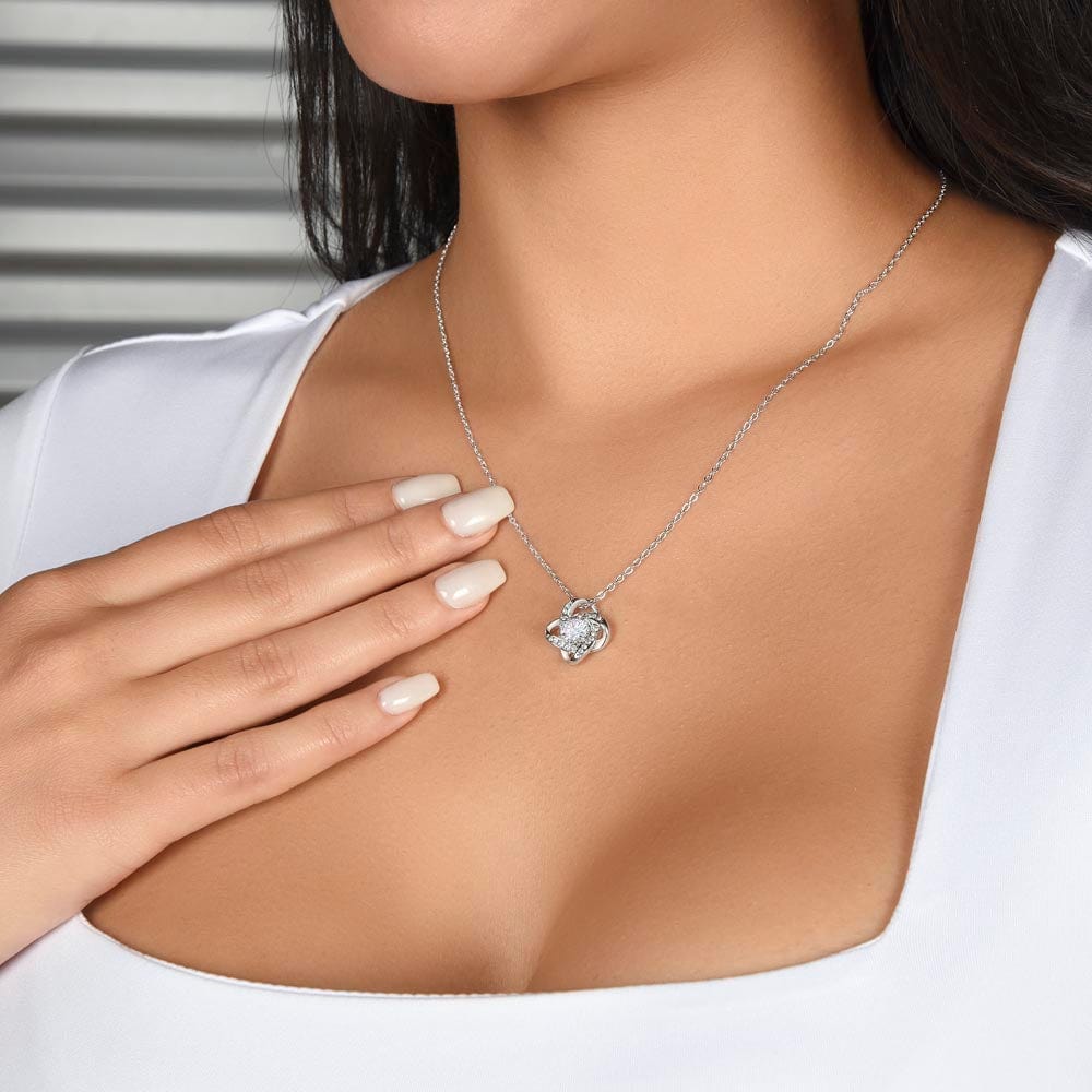 A woman wearing a white gold finish necklace gift, with a knot pendant embellished with premium cubic zirconia crystals.