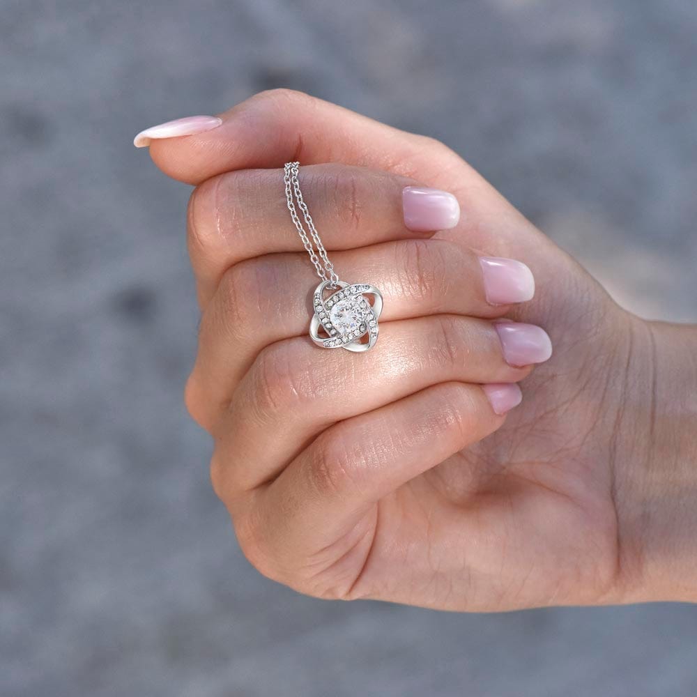 A woman holding a white gold finish necklace gift, with a knot pendant embellished with premium cubic zirconia crystals.