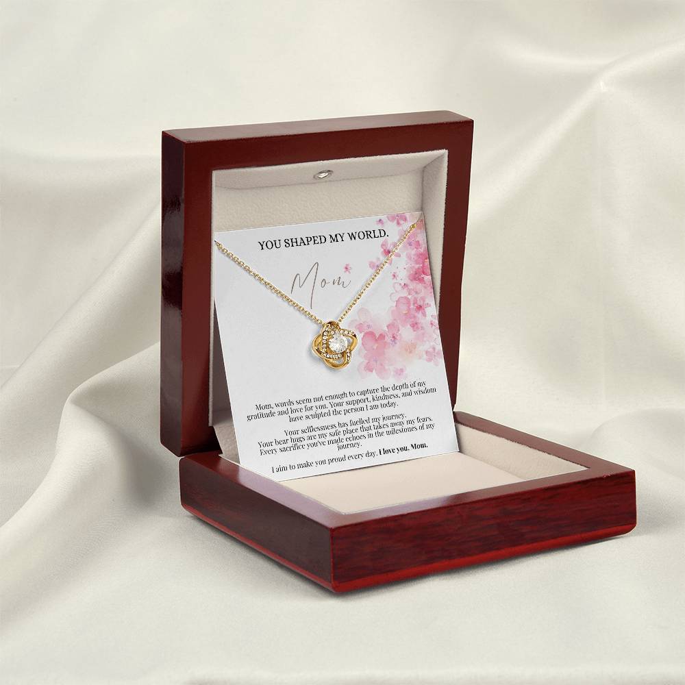 A yellow gold finish necklace gift, with a knot pendant embellished with premium cubic zirconia crystals, and a message card to mom, in a mahogany Jewelry box.