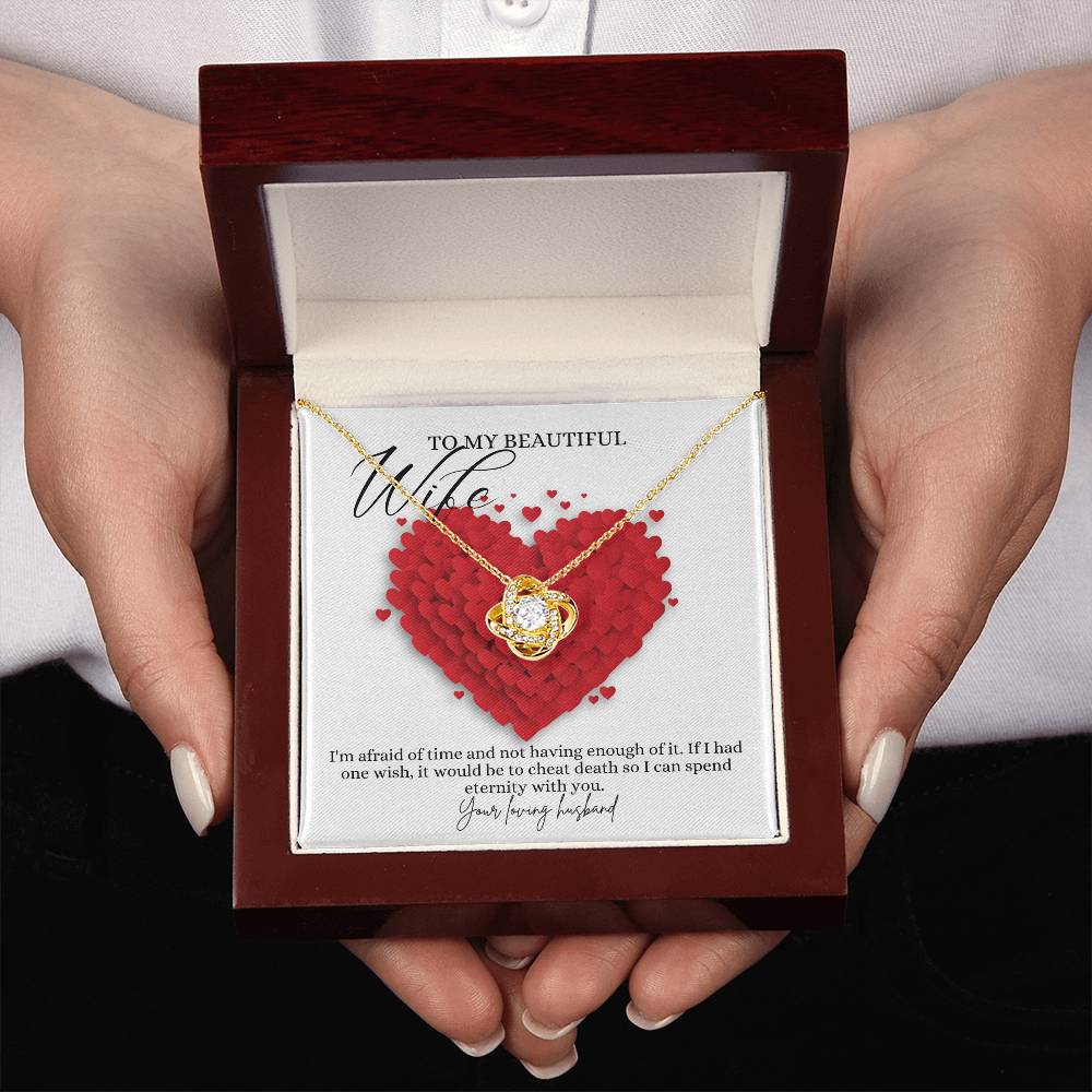 A woman presenting a mahogany jewelry box, a yellow gold finish necklace gift, with a knot pendant embellished with premium cubic zirconia crystals, and a message card to my beautiful wife.