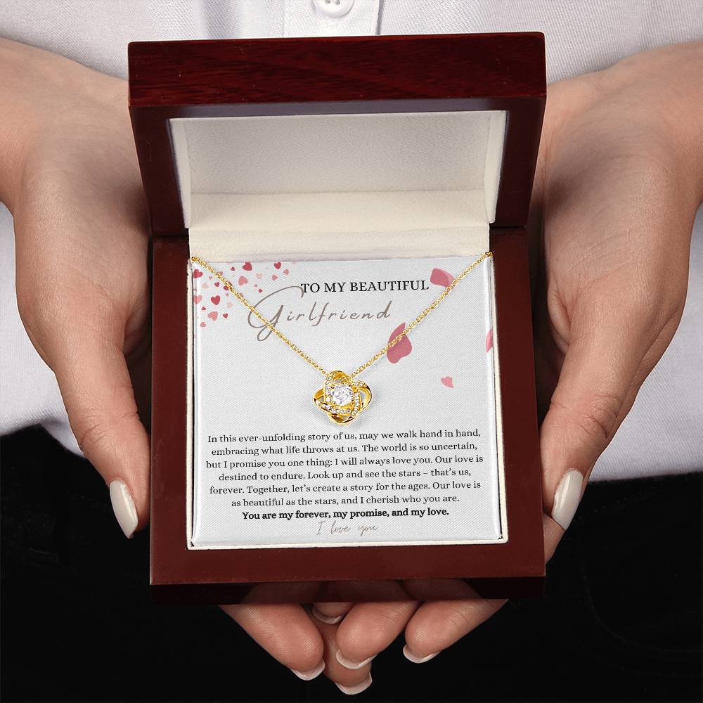 A woman presenting a mahogany jewelry box, a yellow gold finish necklace gift, with a knot pendant embellished with premium cubic zirconia crystals, and a message card to my beautiful girlfriend.