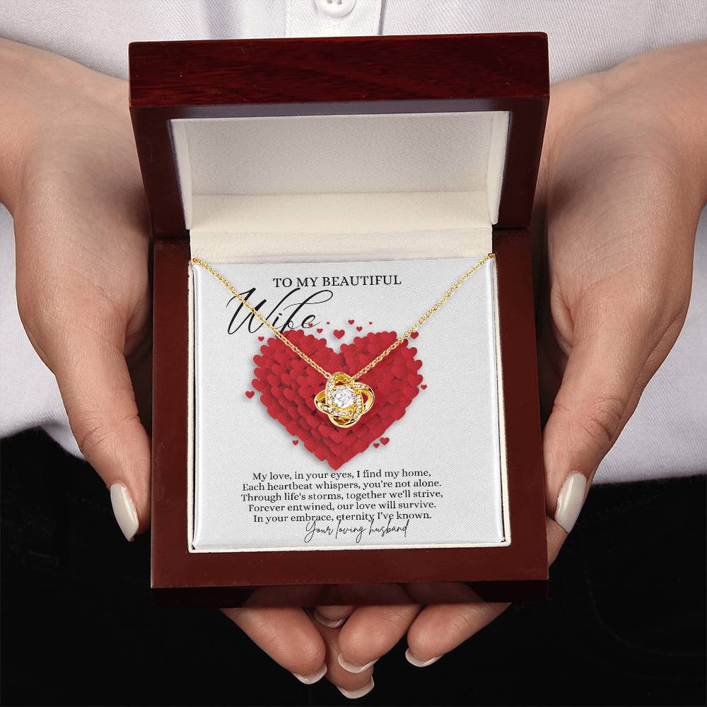 A woman presenting a mahogany jewelry box, with a yellow gold finish necklace gift, with a knot pendant embellished with premium cubic zirconia crystals, and a message card to my beautiful wife.