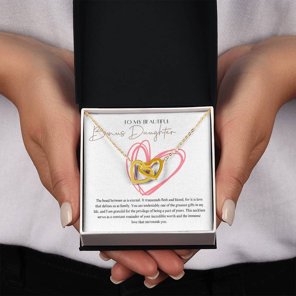 A woman presenting a jewelry box, with a necklace with two connected hearts embellished in cubic zirconia crystals and gold finish, with a message card to my beautiful bonus daughter.
