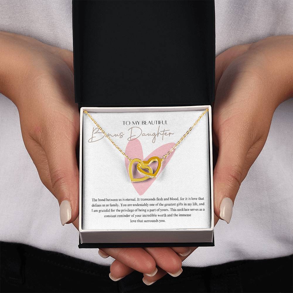 A woman presenting a jewelry box, with a necklace with two connected hearts embellished in cubic zirconia crystals and gold finish, with a message card to my beautiful bonus daughter.