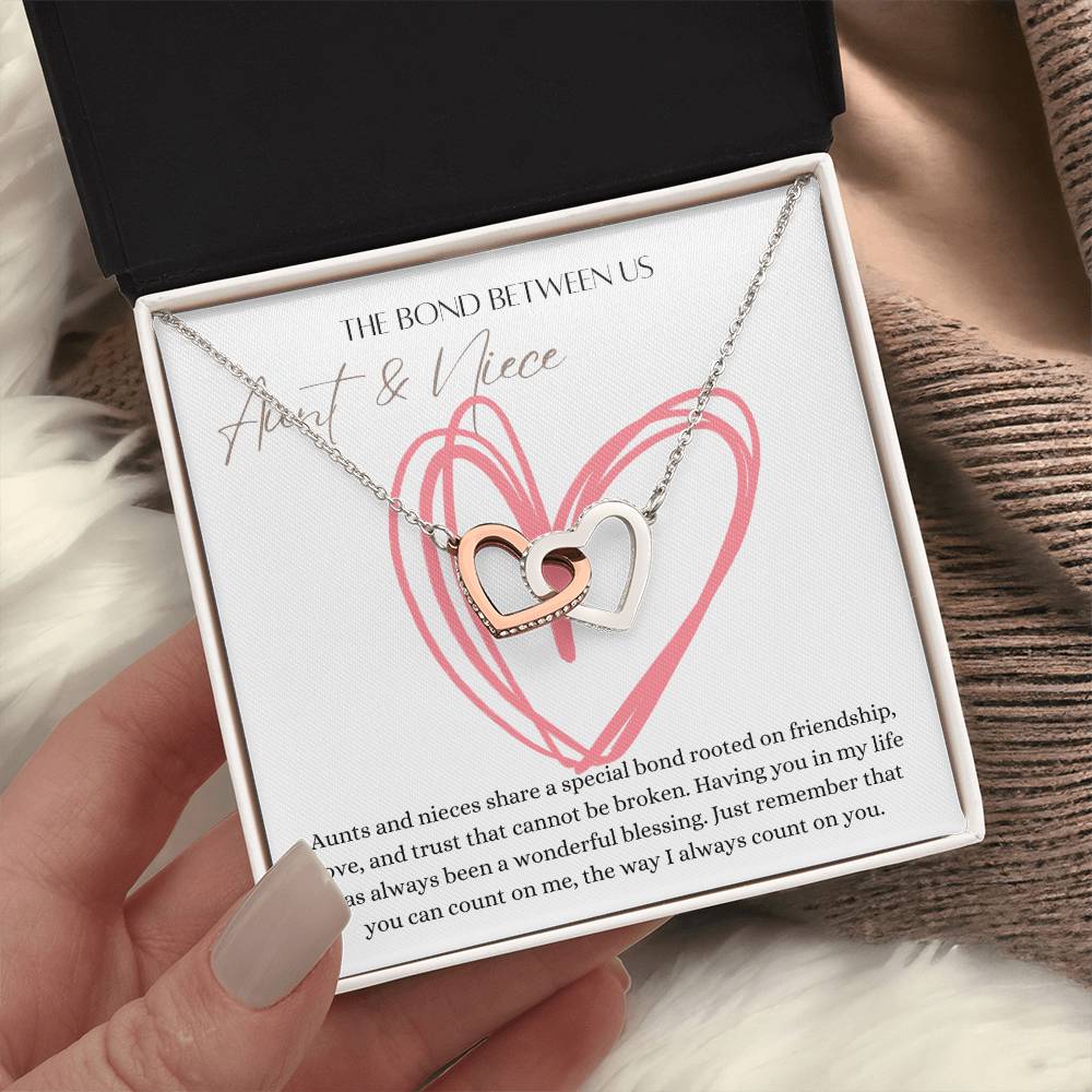 A woman holding a mahogany jewelry box with a necklace with two connected hearts embellished with cubic zirconia crystals with a message card for aunt's and niece's.