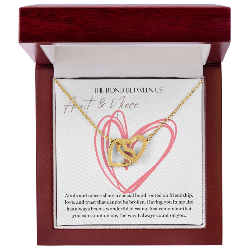 A mahogany Jewelry box with a necklace with two connected hearts embellished with cubic zirconia crystals and a gold finish with a message card for aunt's and niece's.