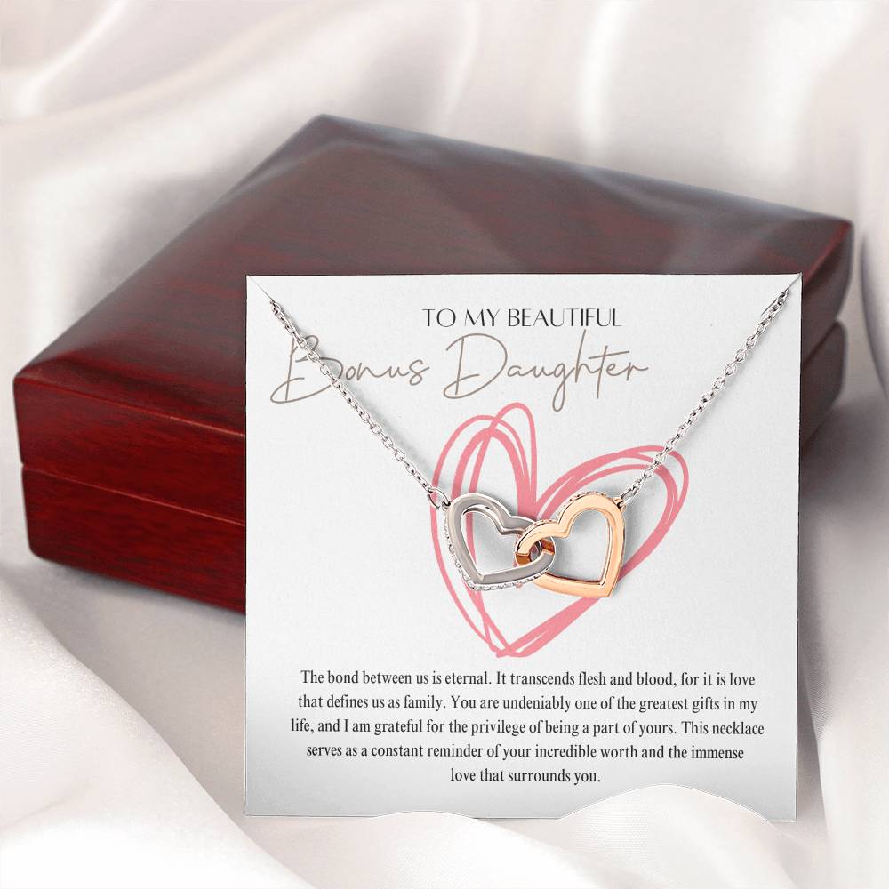 A necklace gift with ribbon shaped pendant with cubic zirconia crystals and white gold finish, with a message card to my beautiful bonus daughter, next to a mahogany Jewelry box.