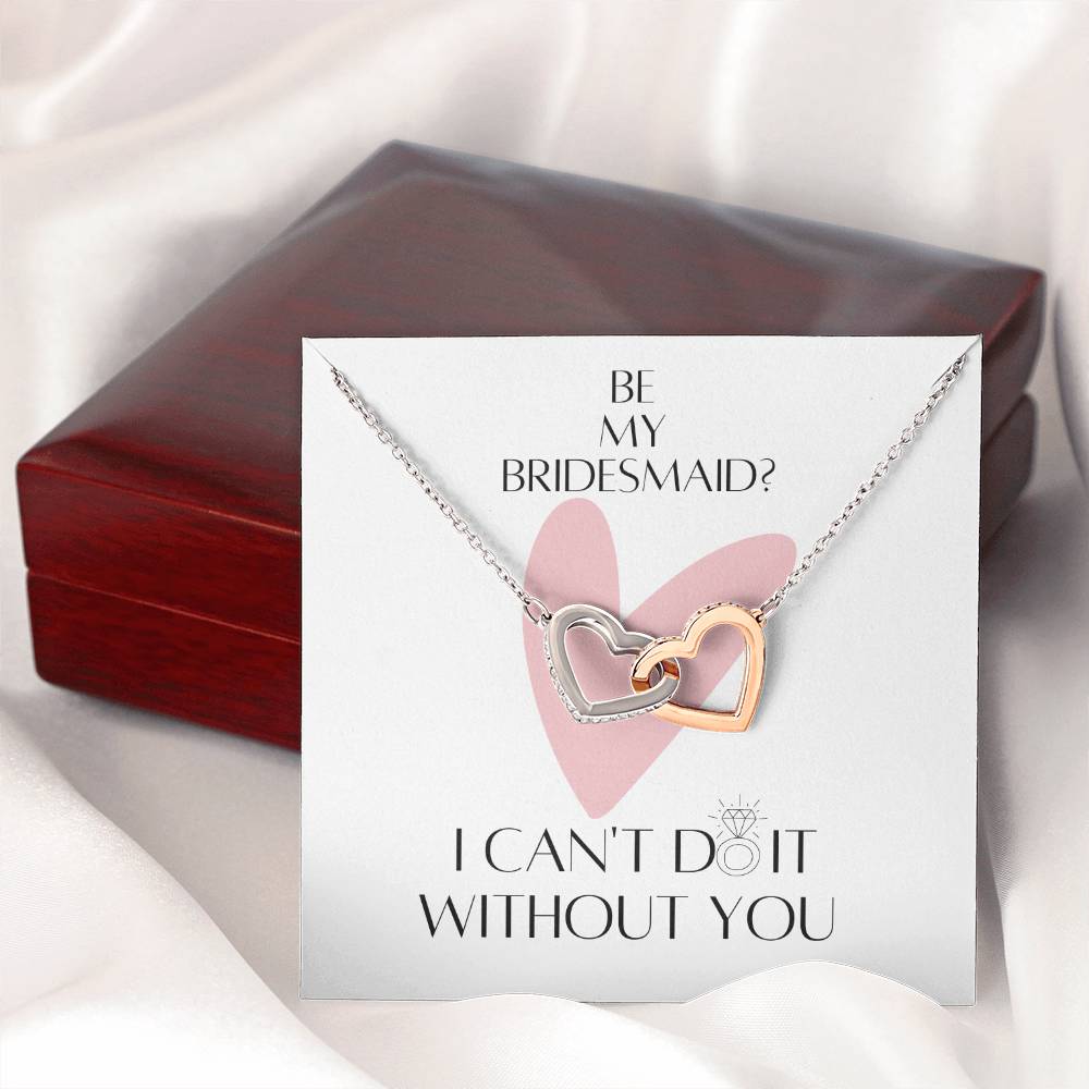 A necklace with two connected hearts embellished with cubic zirconia crystals with a message card for bridesmaids, next to a mahogany gift box.