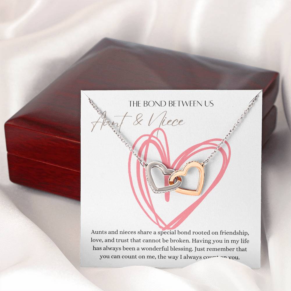 A necklace with two connected hearts embellished with with cubic zirconia crystals  with a message card for aunt's and niece's next to a mahogany gift box.