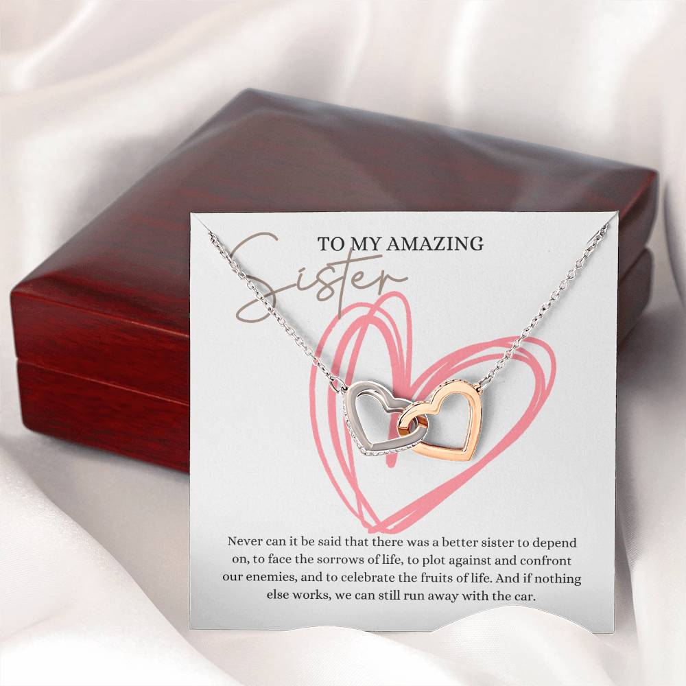 A necklace gift with ribbon shaped pendant with cubic zirconia crystals and white gold finish, with a message card to my amazing sister, next to a mahogany Jewelry box.