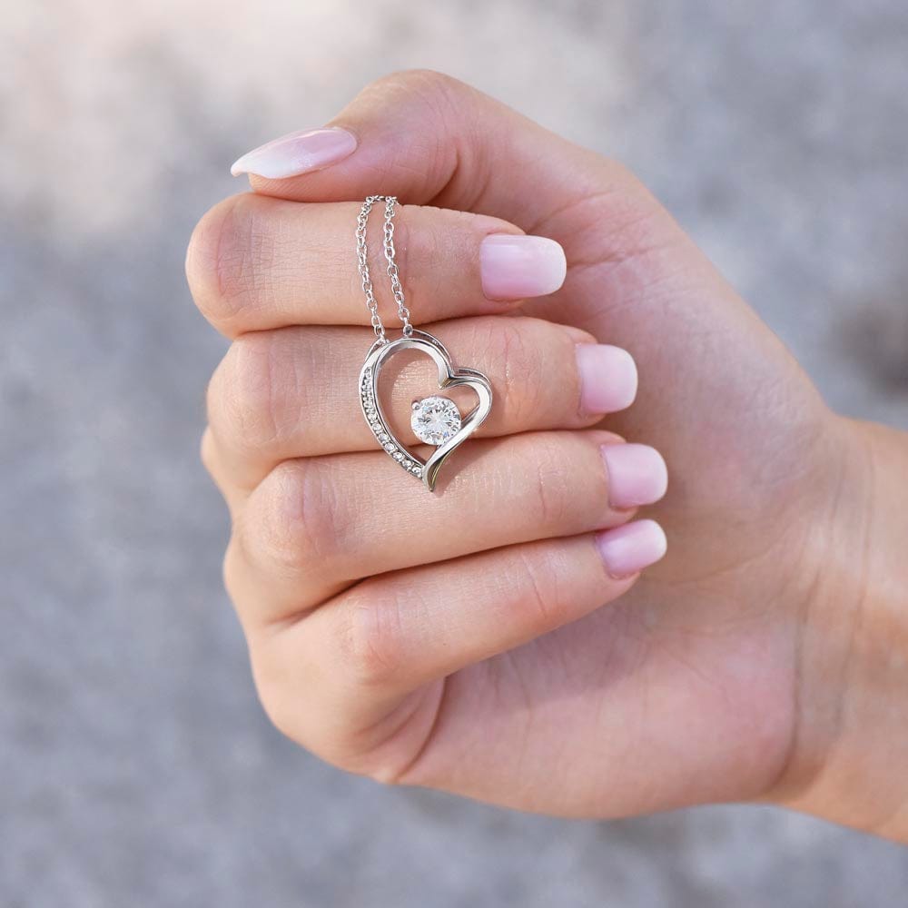 A woman holding with a white gold finish necklace gift, featuring a stunning 6.5mm CZ crystal surrounded by a polished heart pendant embellished with smaller crystals.