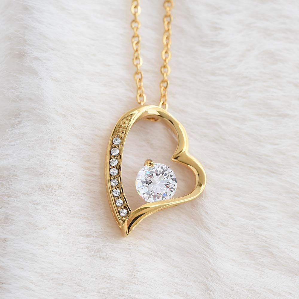 A yellow gold finish necklace gift, featuring a stunning 6.5mm CZ crystal surrounded by a polished heart pendant embellished with smaller crystals, laying on a white furry carpet.