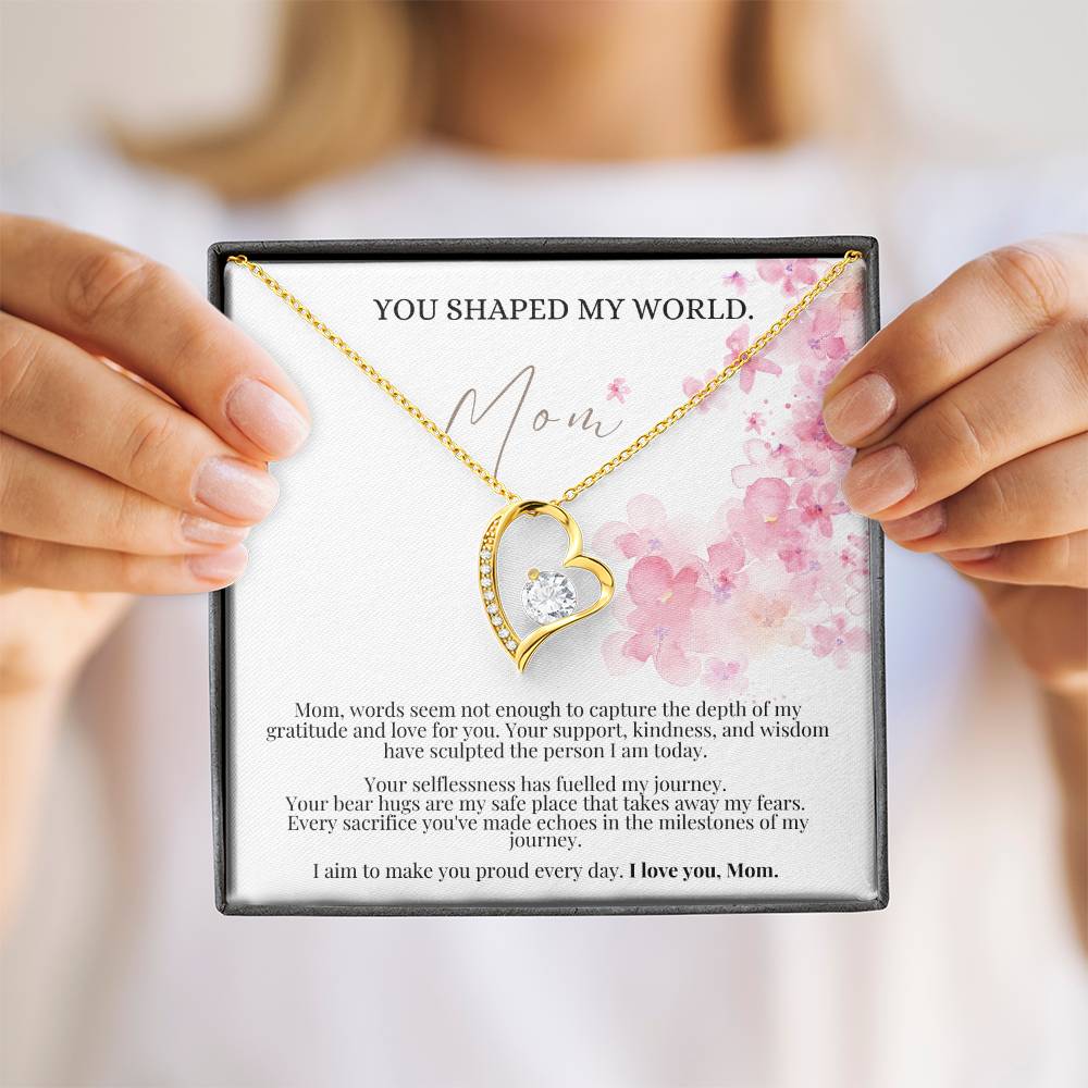 A woman presenting a jewelry box, with a yellow gold finish necklace gift, featuring a stunning 6.5mm CZ crystal surrounded by a polished heart pendant embellished with smaller crystals.