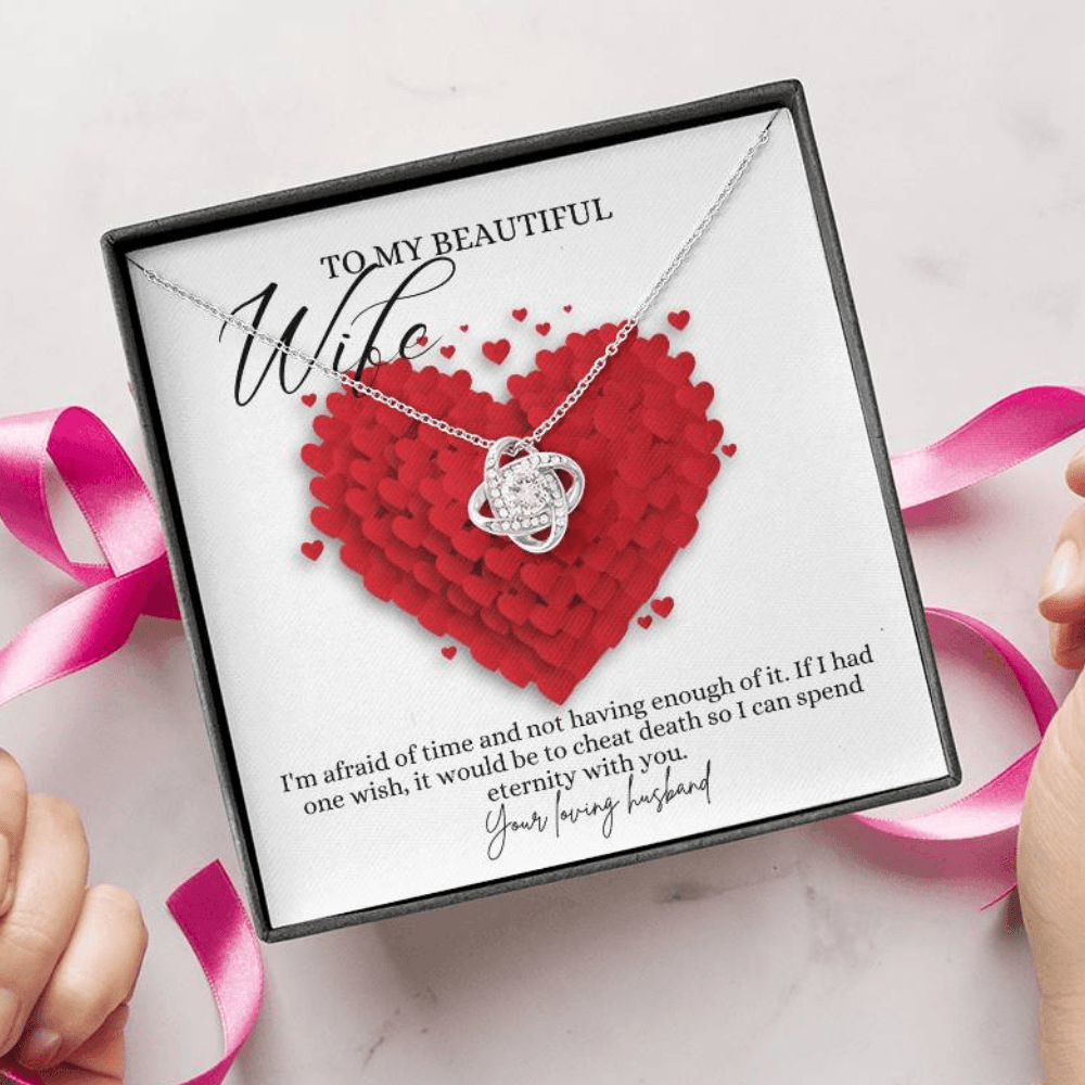 A person unwrapping a jewelry box with a white gold finish necklace gift, with a knot pendant embellished with premium cubic zirconia crystals, and a message card to my beautiful wife.