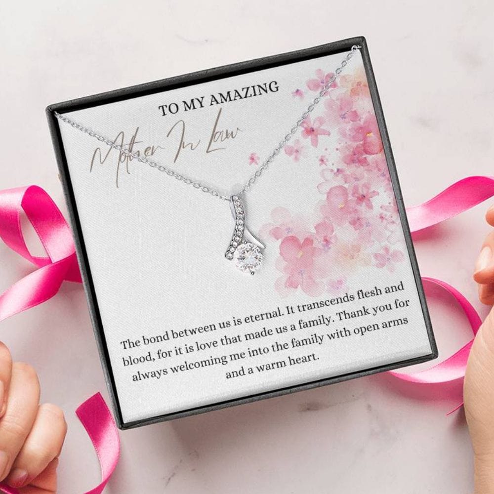 A person unwrapping a necklace gift with ribbon shaped pendant with cubic zirconia crystals and white gold finish, with a message card to my mother in law.